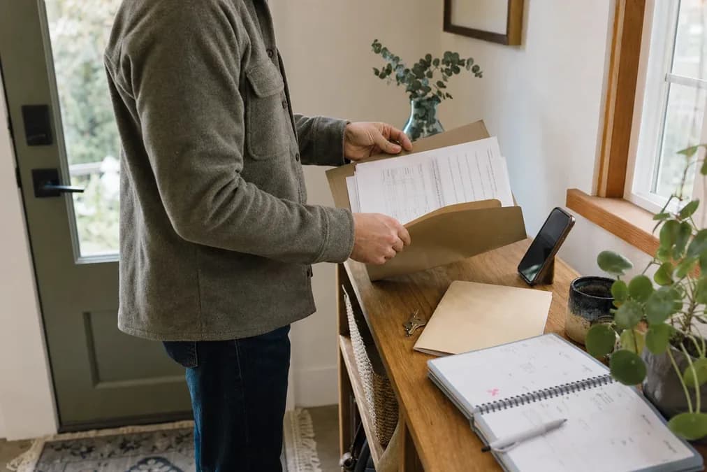 A person works through online divorce paperwork at a kitchen table with printed forms nearby.